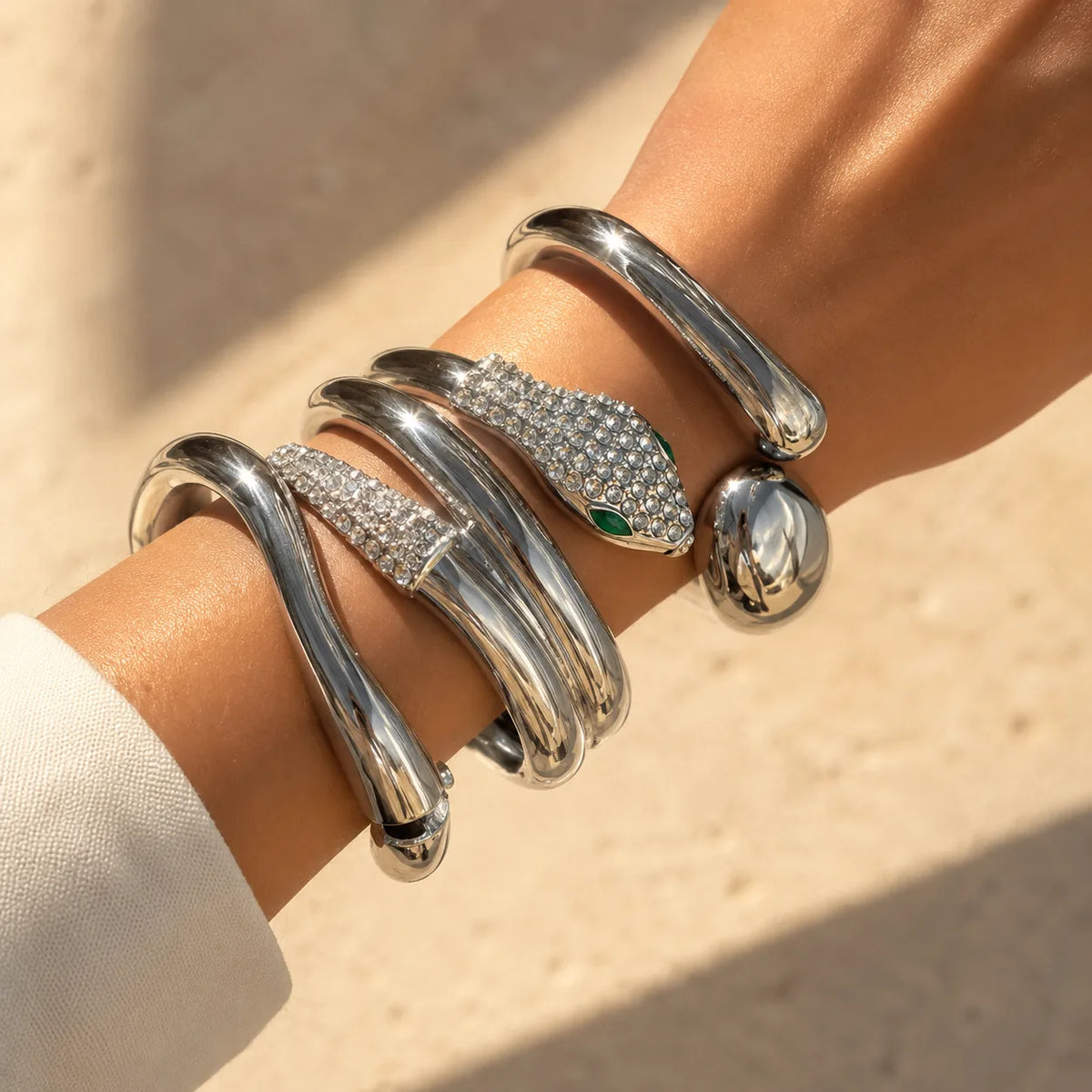 Silver snake-shaped bracelet with gemstone eyes on a wrist against a beige background