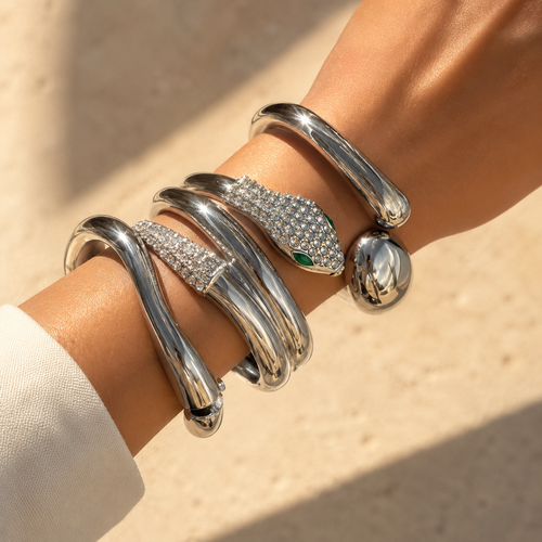 Silver snake-shaped bracelet with gemstone eyes on a wrist against a beige background