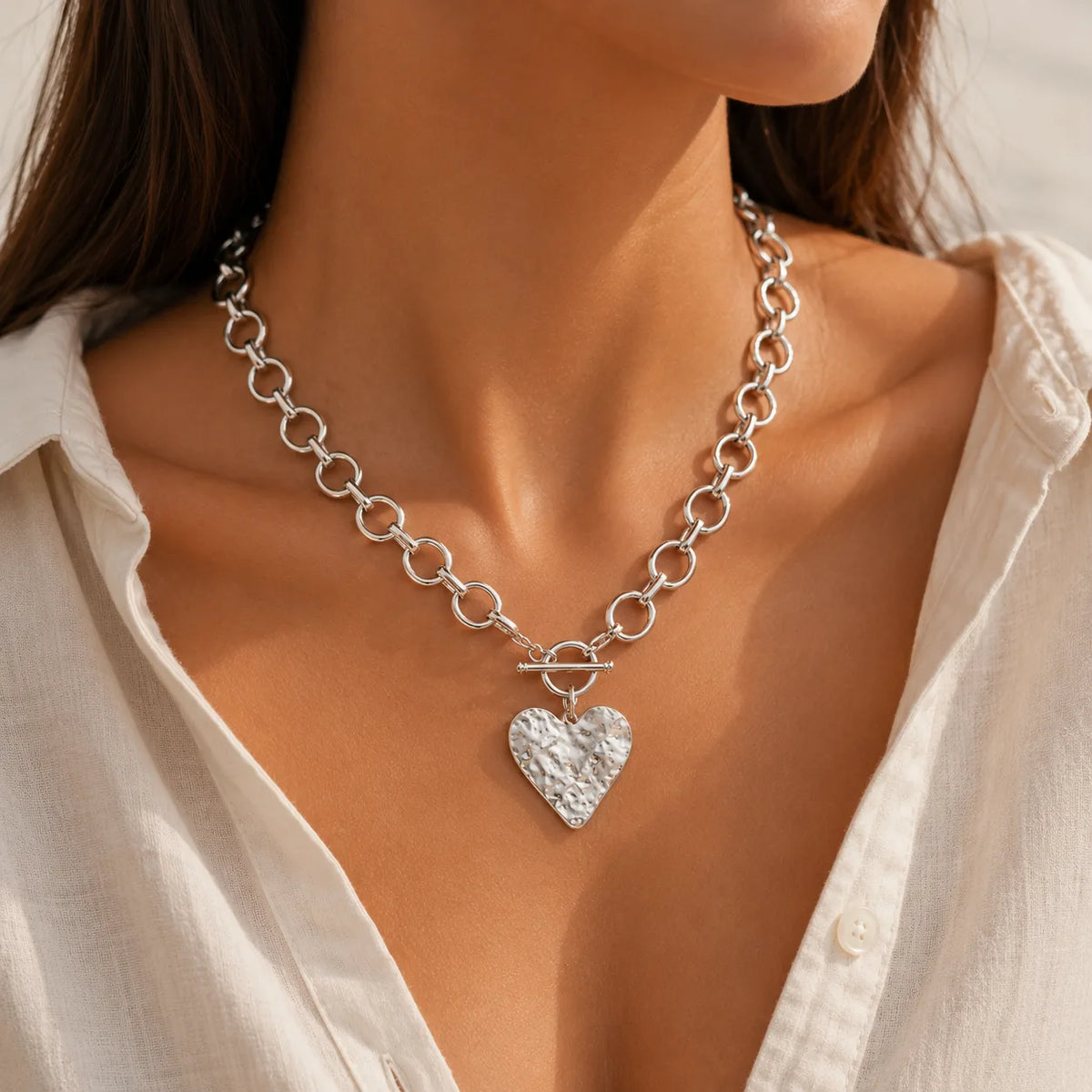 Silver chain necklace with a heart pendant worn by a person in a white shirt.