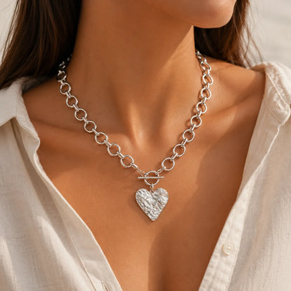 Silver chain necklace with a heart pendant worn by a person in a white shirt.
